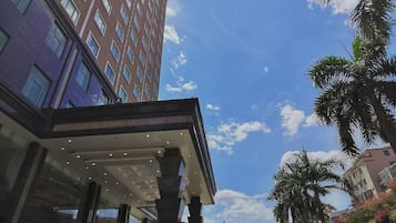 A hotel entrance with a covered walkway, a parking area, and a tall building in the background.
