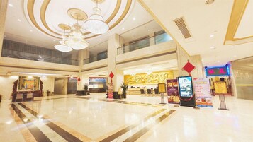 Eine geräumige Lobby mit hoher Decke, Kronleuchtern und einem Empfangsbereich mit Informationsbildschirmen.