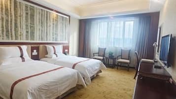 A hotel room with two beds, a desk, a chair, a television, and a large window with curtains.