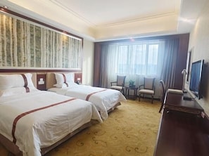 Habitación de hotel con dos camas, un escritorio, una silla, un televisor y un ventanal con cortinas.