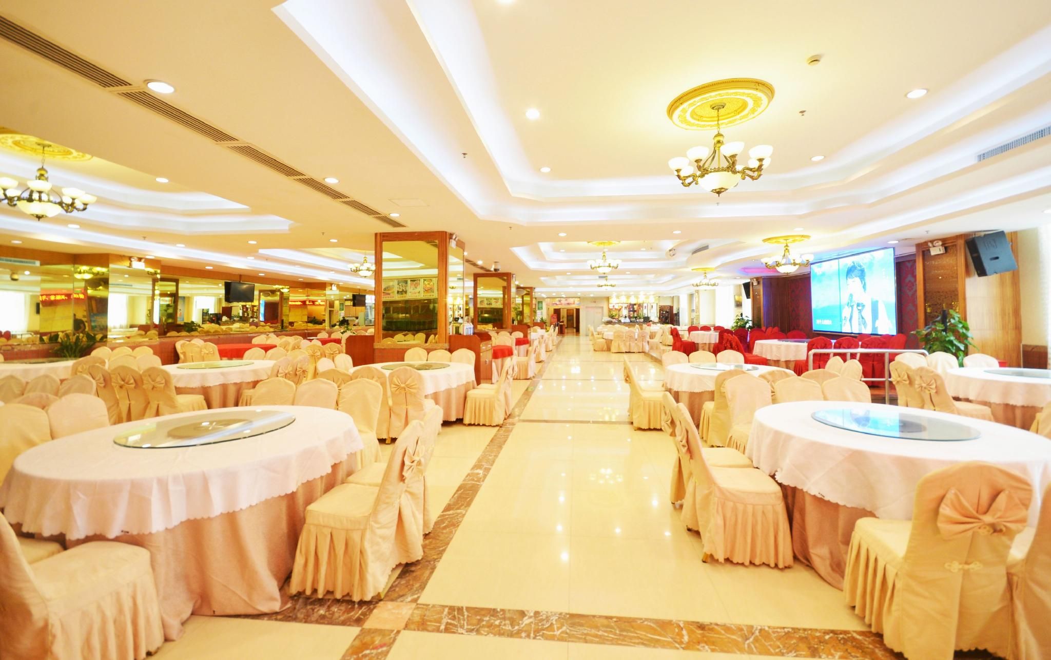 Un salón de banquetes con mesas y sillas redondas, una pantalla grande y candelabros.