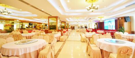 A banquet hall with round tables and chairs, a large screen, and chandeliers.