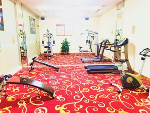 Ein Fitnessraum mit unterschiedlichen Trainingsgeräten, darunter Laufbändern und Kraftmaschinen, auf einem roten Teppich mit Muster.