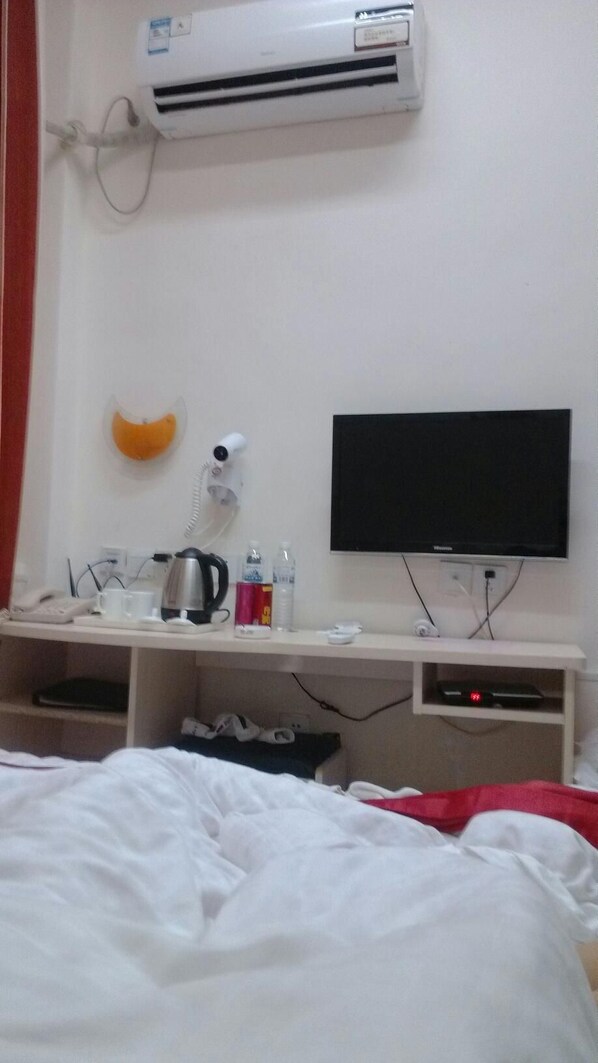 A hotel room with a bed, a desk with a television, a kettle, a cup, and a bottle. - Thank You Hotel (Qingdao)