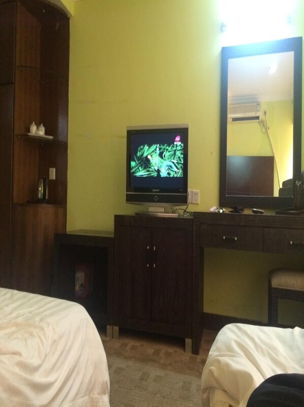 A hotel room with a television on a wooden cabinet, a mirror on the wall, and two beds. - Wanma Hotel (Guangzhou)