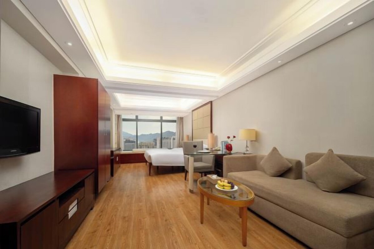 Une chambre d’hôtel équipée d’une télévision à écran plat, d’un canapé, d’un bureau et d’une fenêtre donnant sur la ville.