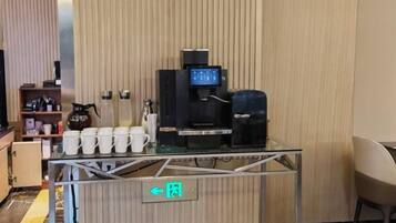 A coffee station with a coffee machine, cups, and a sign indicating a restroom.