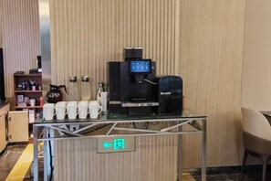 Un espace dédié au café, équipé d’une machine à café, de tasses et d’un panneau indiquant l’emplacement des toilettes.