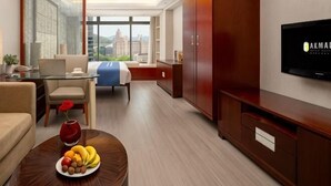 Hotelkamer met een bed, een televisie, een bureau, een stoel, een bijzettafeltje met fruit en uitzicht op de stad.