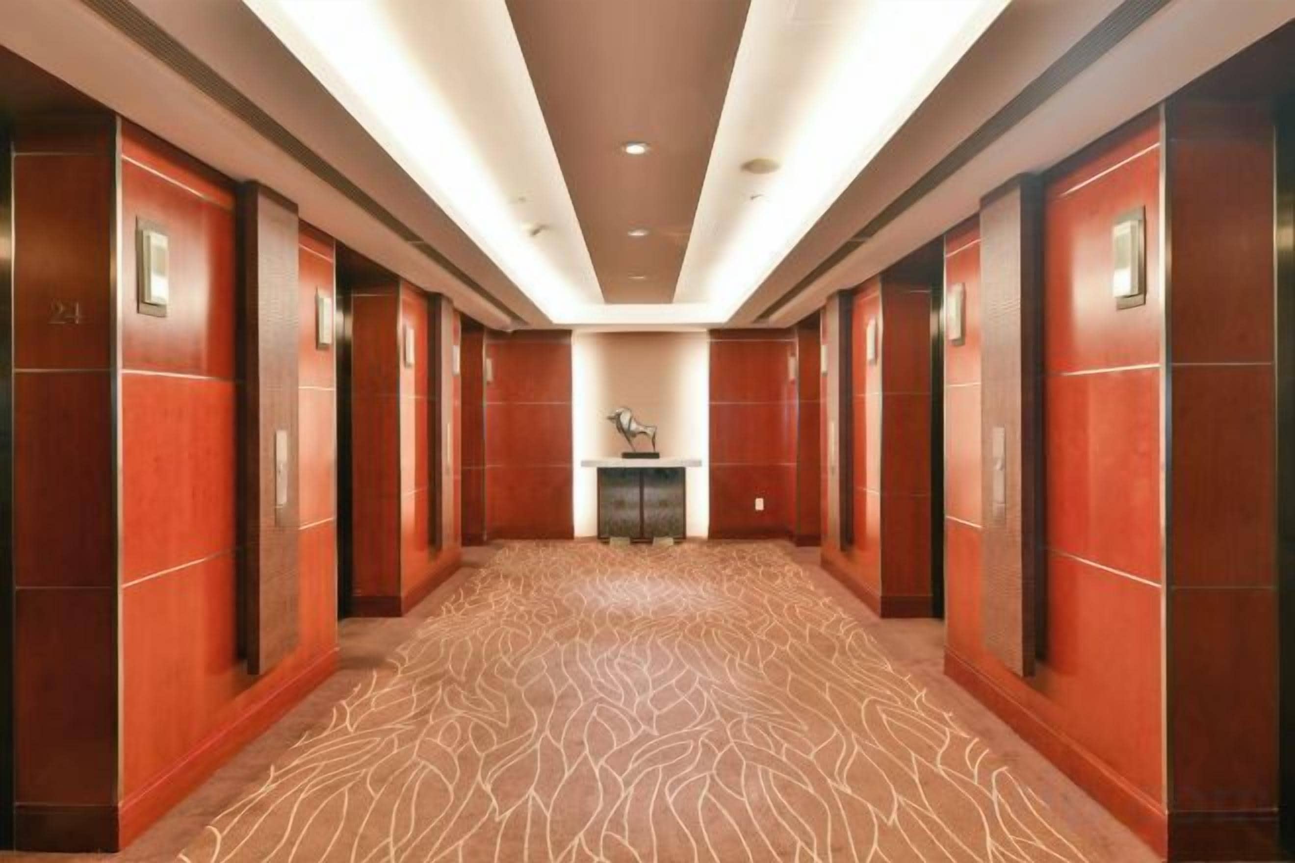 Een hotelgang met een kamerjas patroon, houten wanden en een centrale lift.