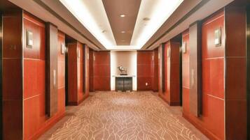 Een hotelgang met een kamerjas patroon, houten wanden en een centrale lift.