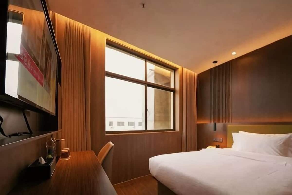 A hotel room with a bed, a desk, a TV, and a window.