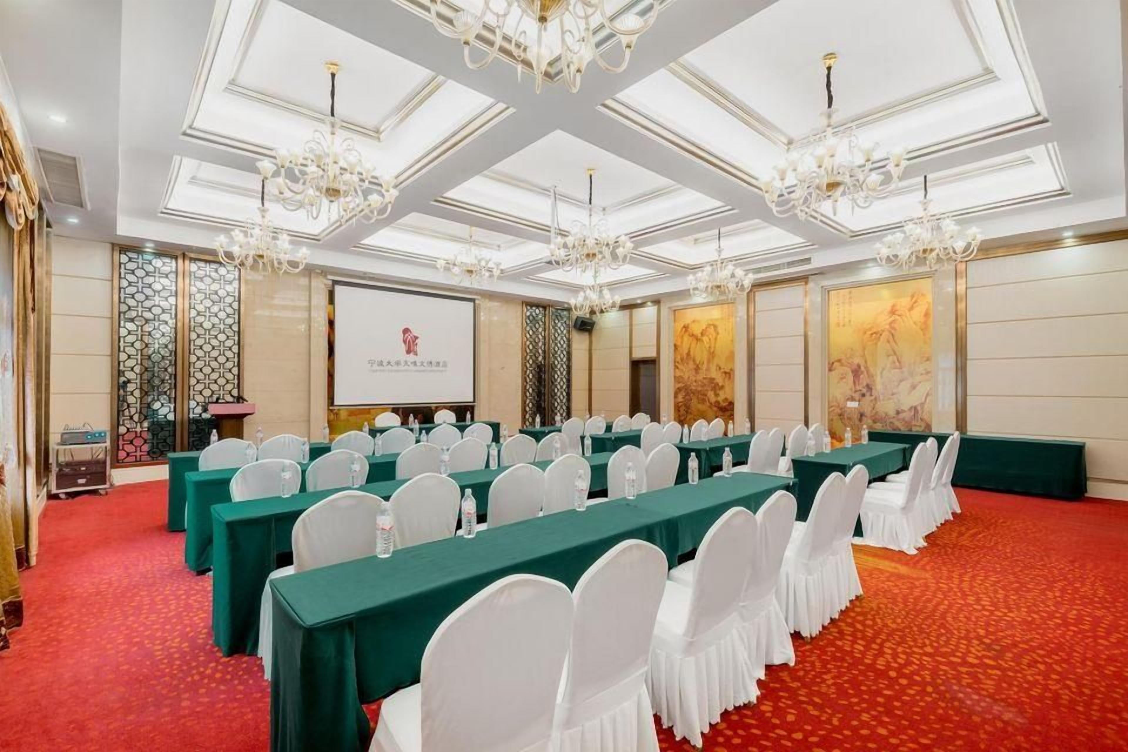 A conference room with long tables, white chairs, and chandeliers.