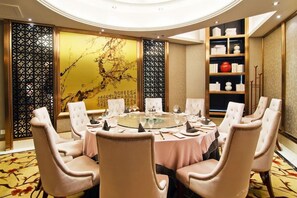 A round table with chairs, a decorative wall, and a bookshelf with books and vases.