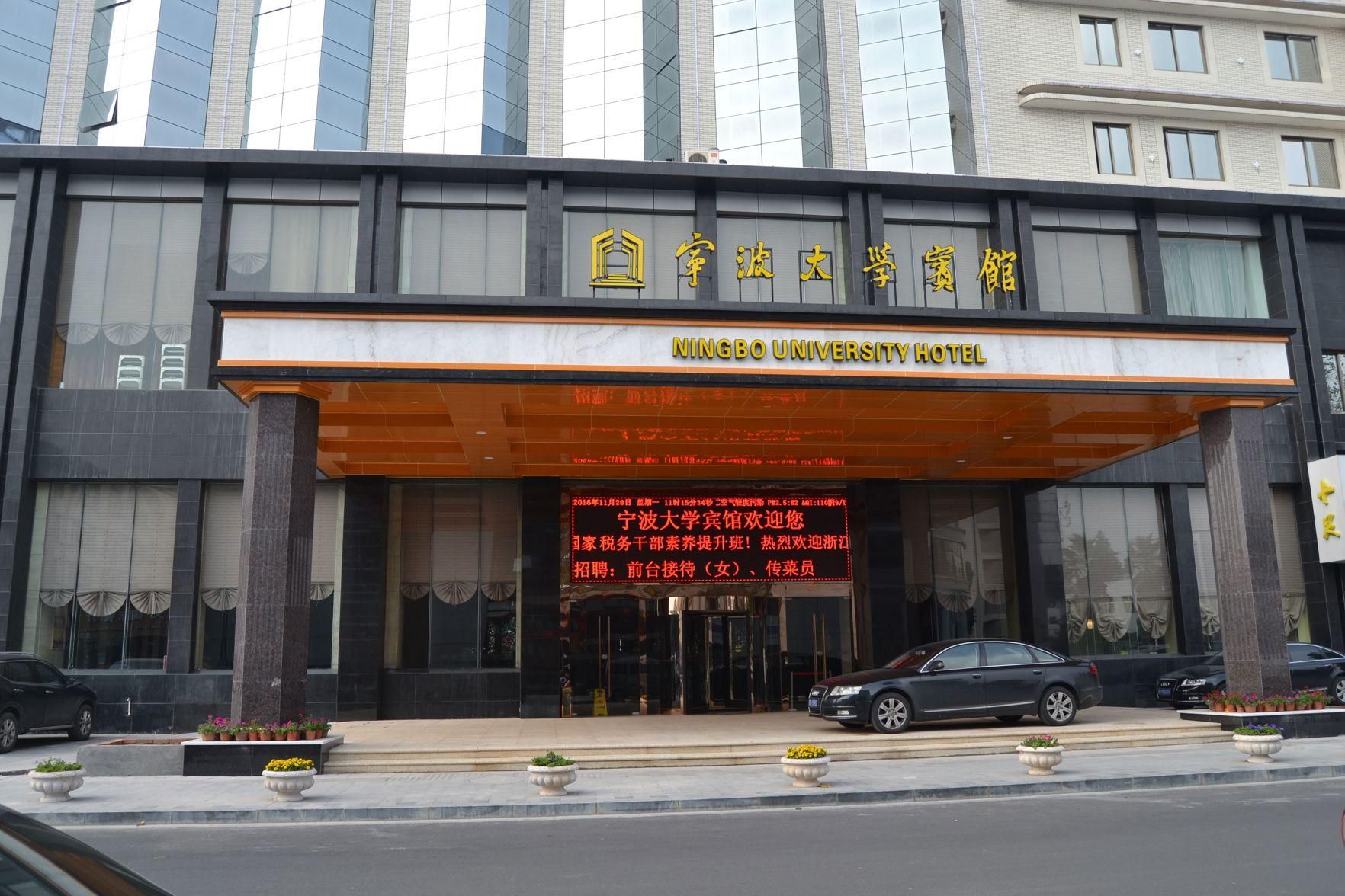 Entrada de hotel com uma grande placa em caracteres chineses e o nome em inglês 'Ningbo University Hotel'.