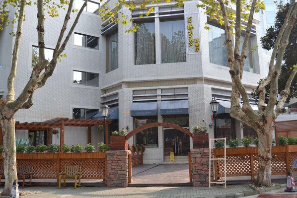 A modern building with a brick facade, large windows, and a wooden pergola with seating.