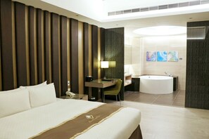 Habitación de hotel con una cama grande, un escritorio con una silla, una lámpara de escritorio, un teléfono, un baño con bañera y un amplio ventanal con una obra de arte.