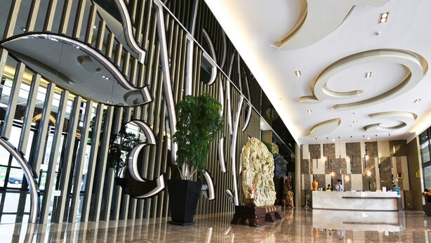 Een moderne lobby met een receptiebalie, een groot decoratief beeld en een potplant.