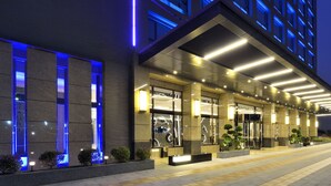 Een moderne hotelingang met een overdekte doorgang, verlichte borden en een verzorgd uiterlijk.