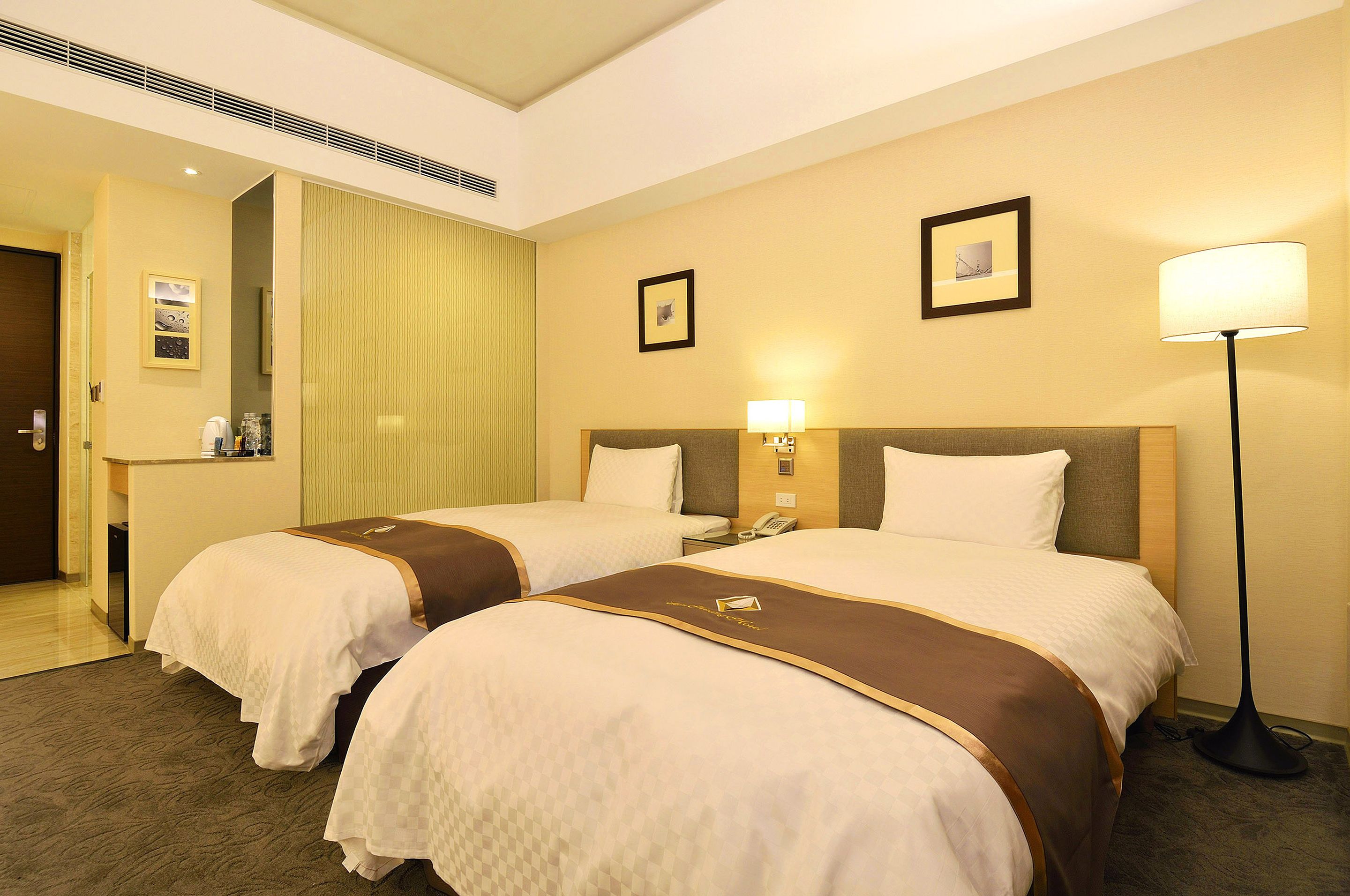 A hotel room with two beds, a desk, a lamp, and a mirror.