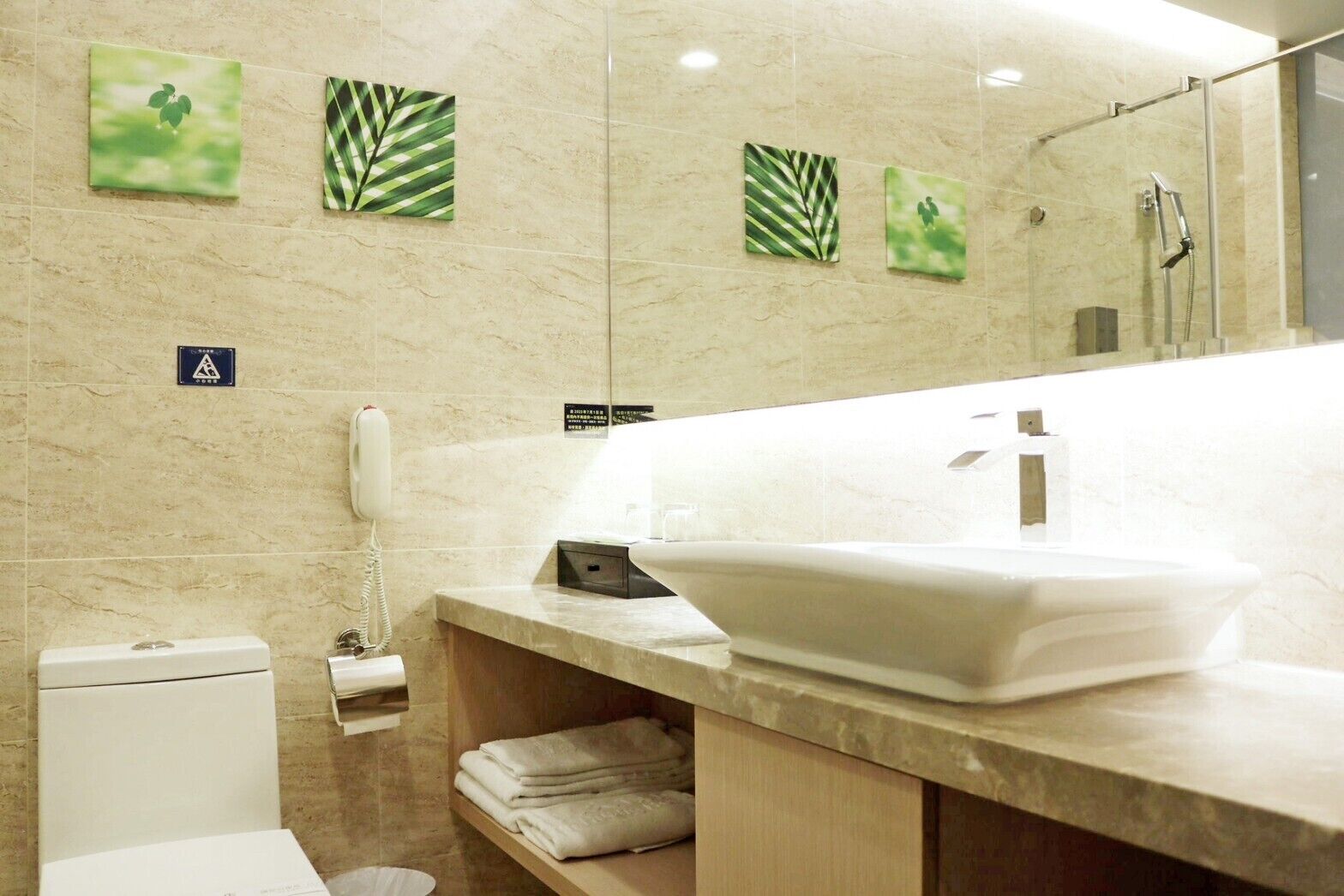 A modern bathroom with a large sink, a mirror, and a shower. There are towels on a shelf and a toilet.