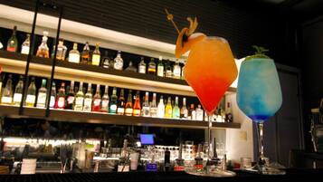 Angolo bar con due cocktail decorati con spiedini di frutta, diverse bottiglie sugli scaffali e un bancone con bicchieri e utensili.