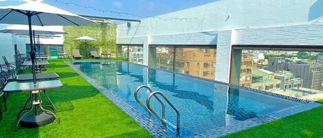 Piscina no terraço com grama sintética, área de estar externa e vista para a cidade.