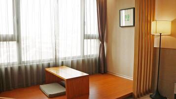 A room with a wooden desk, a cushioned bench, a standing lamp, and sheer curtains.