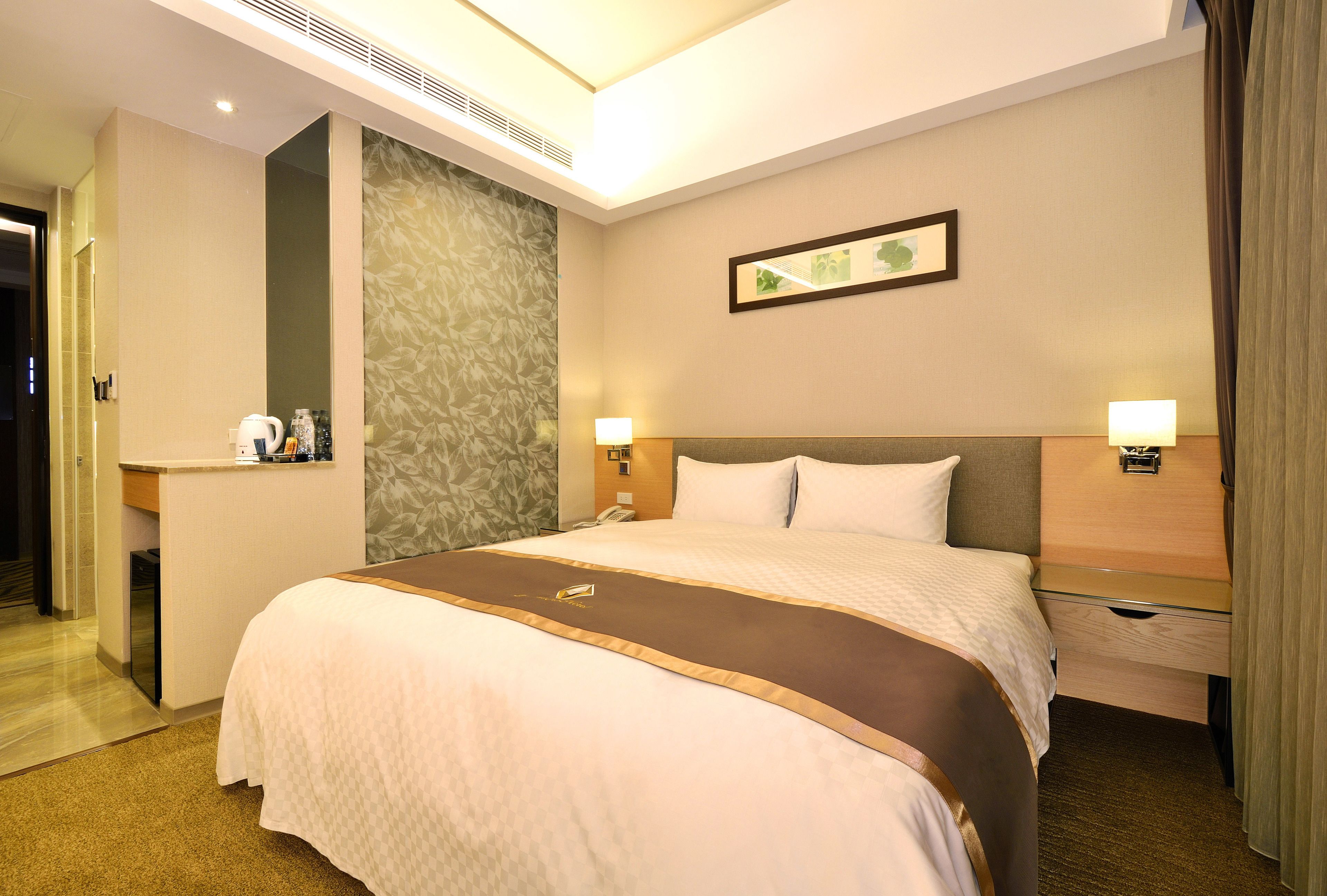 A hotel room with a large bed, bedside tables, a desk with a telephone, and a mirror.