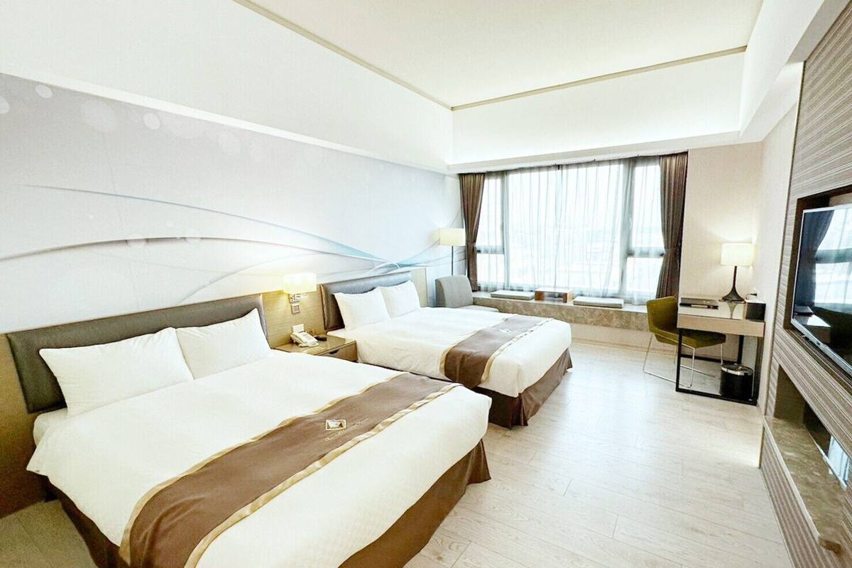Une chambre d’hôtel avec deux lits, un bureau, une chaise, une télévision et une fenêtre avec des rideaux.