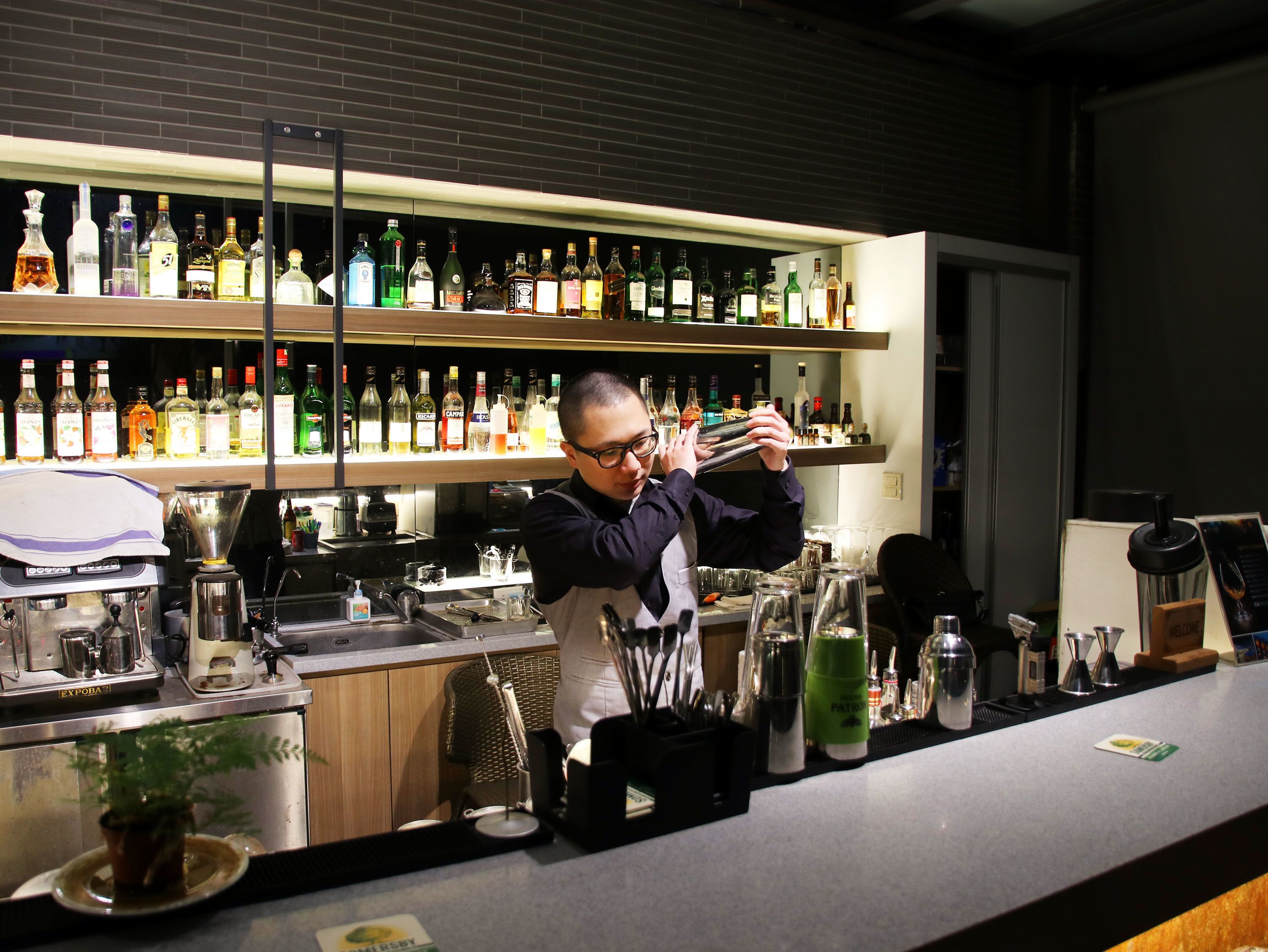 A bar area with a bartender preparing drinks, shelves with various liquor bottles, and bar equipment.