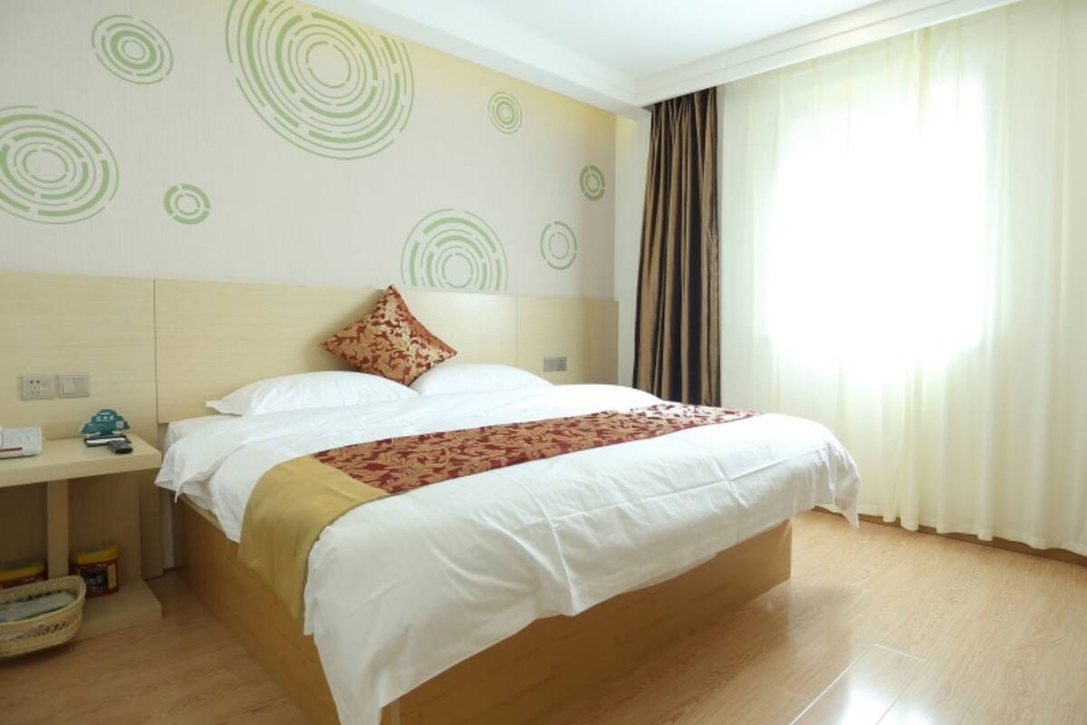 A hotel room with a bed, a nightstand, a lamp, and a window with curtains.