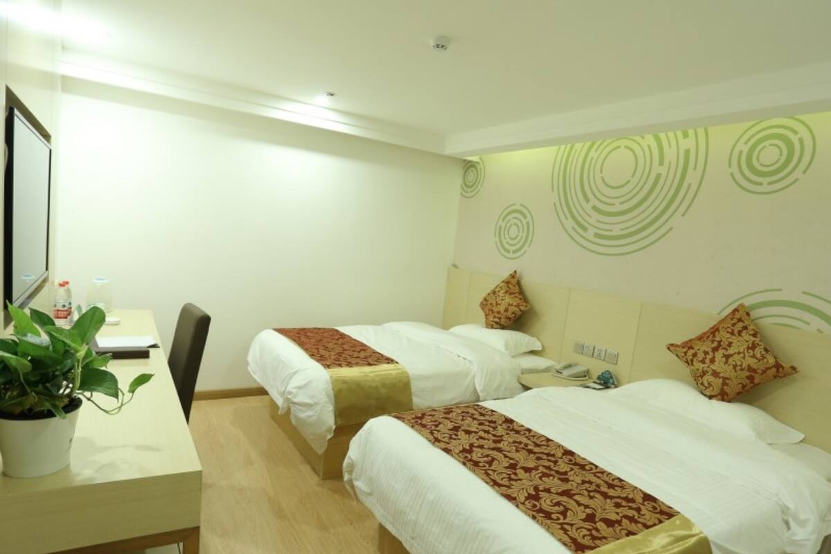 A hotel room with two beds, a desk, a chair, a potted plant, and a wall with circular patterns.