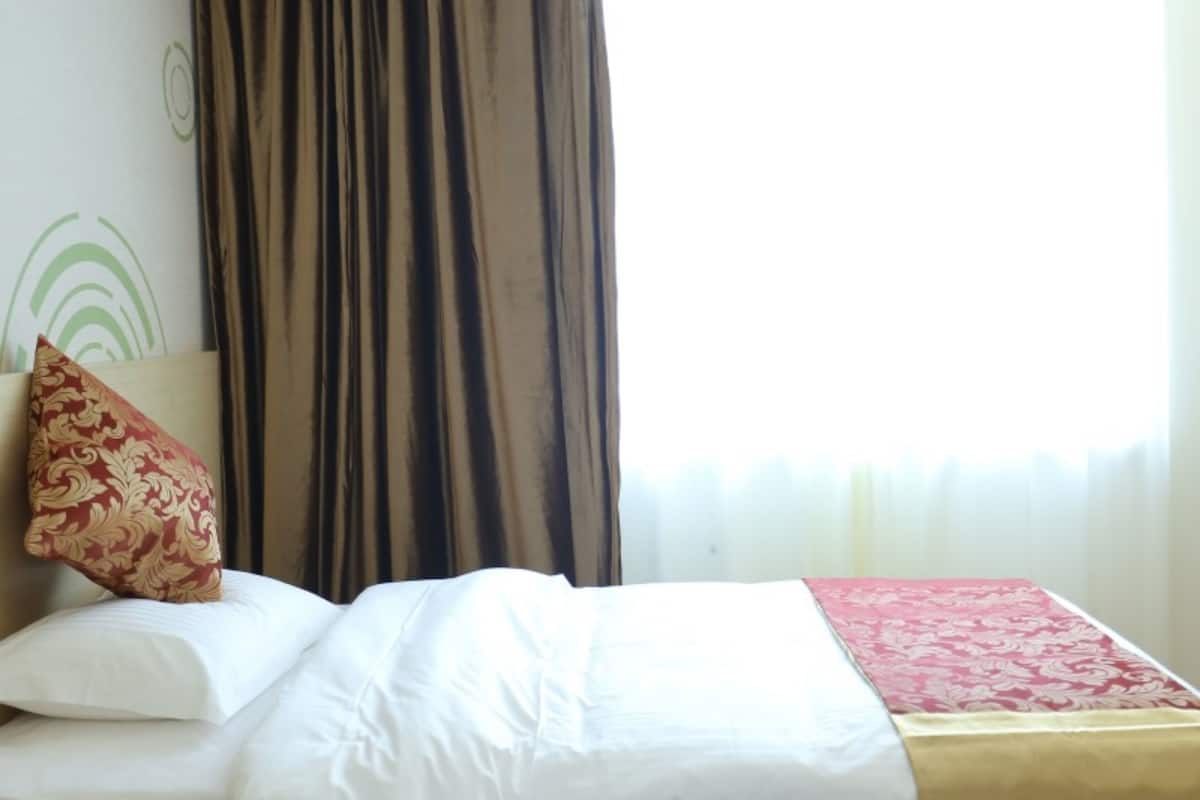 A hotel room with a bed, a red patterned pillow, a white comforter, and a red and gold bedspread.