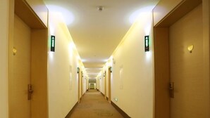 Un pasillo de hotel con puertas a ambos lados, iluminado por luces del techo y con alfombra de diseño circular.