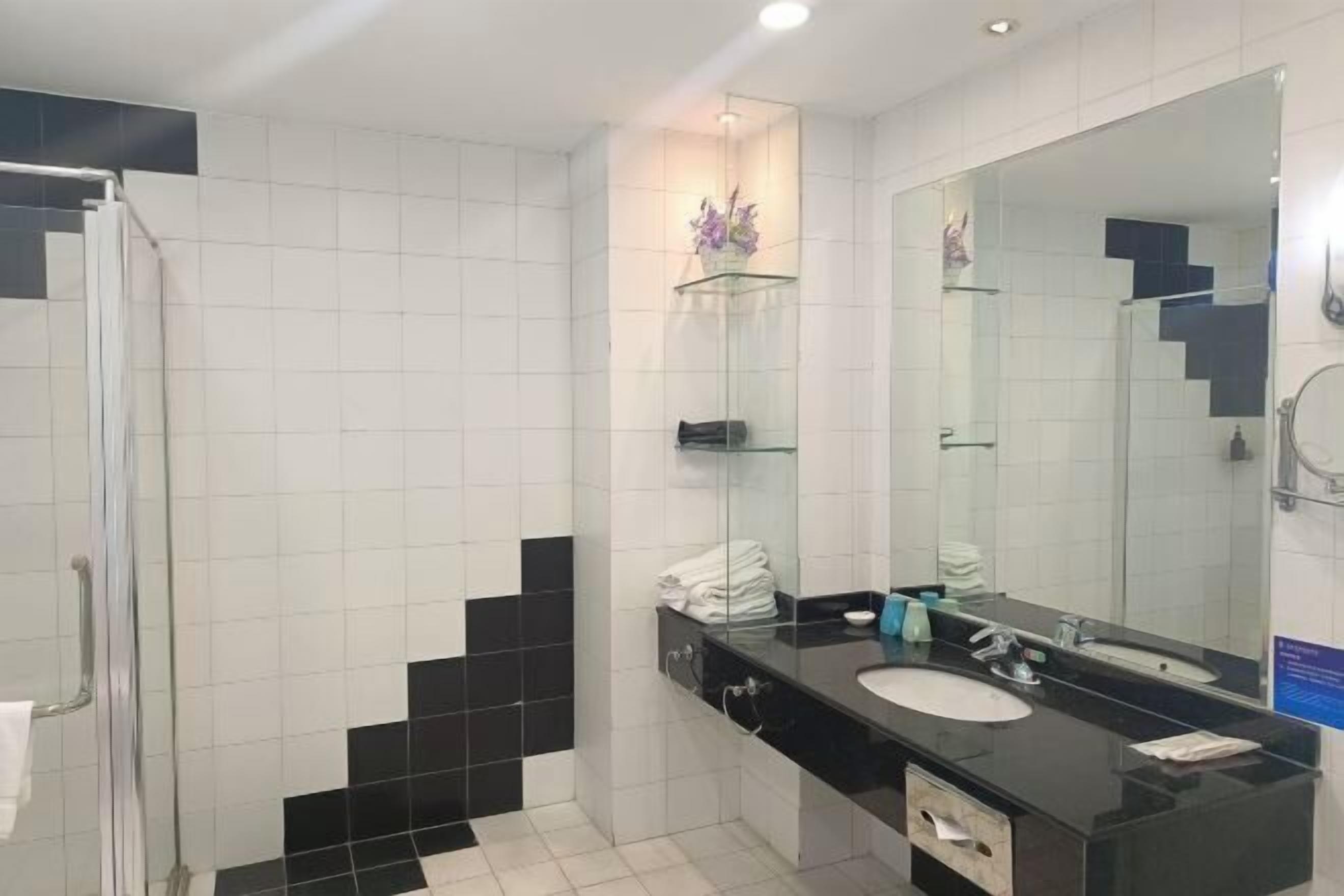 Une salle de bain moderne avec une douche à l’italienne en verre, un mur recouvert de carreaux noirs et blancs, un grand miroir et un plan de toilette noir avec un lavabo.