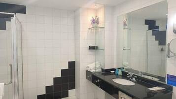 Une salle de bain moderne avec une douche à l’italienne en verre, un mur recouvert de carreaux noirs et blancs, un grand miroir et un plan de toilette noir avec un lavabo.