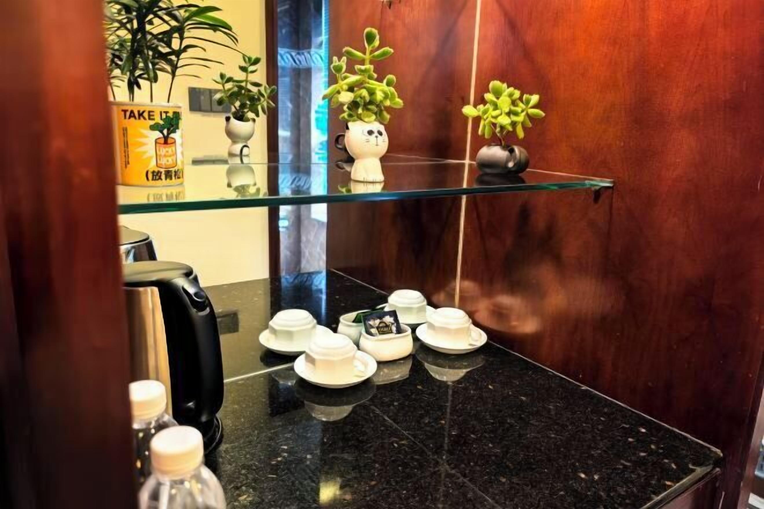 A hotel room with a black marble countertop, a glass shelf with potted plants, and a coffee machine.