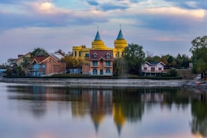 A large building with multiple towers, a reflection in a body of water, and a clear sky.