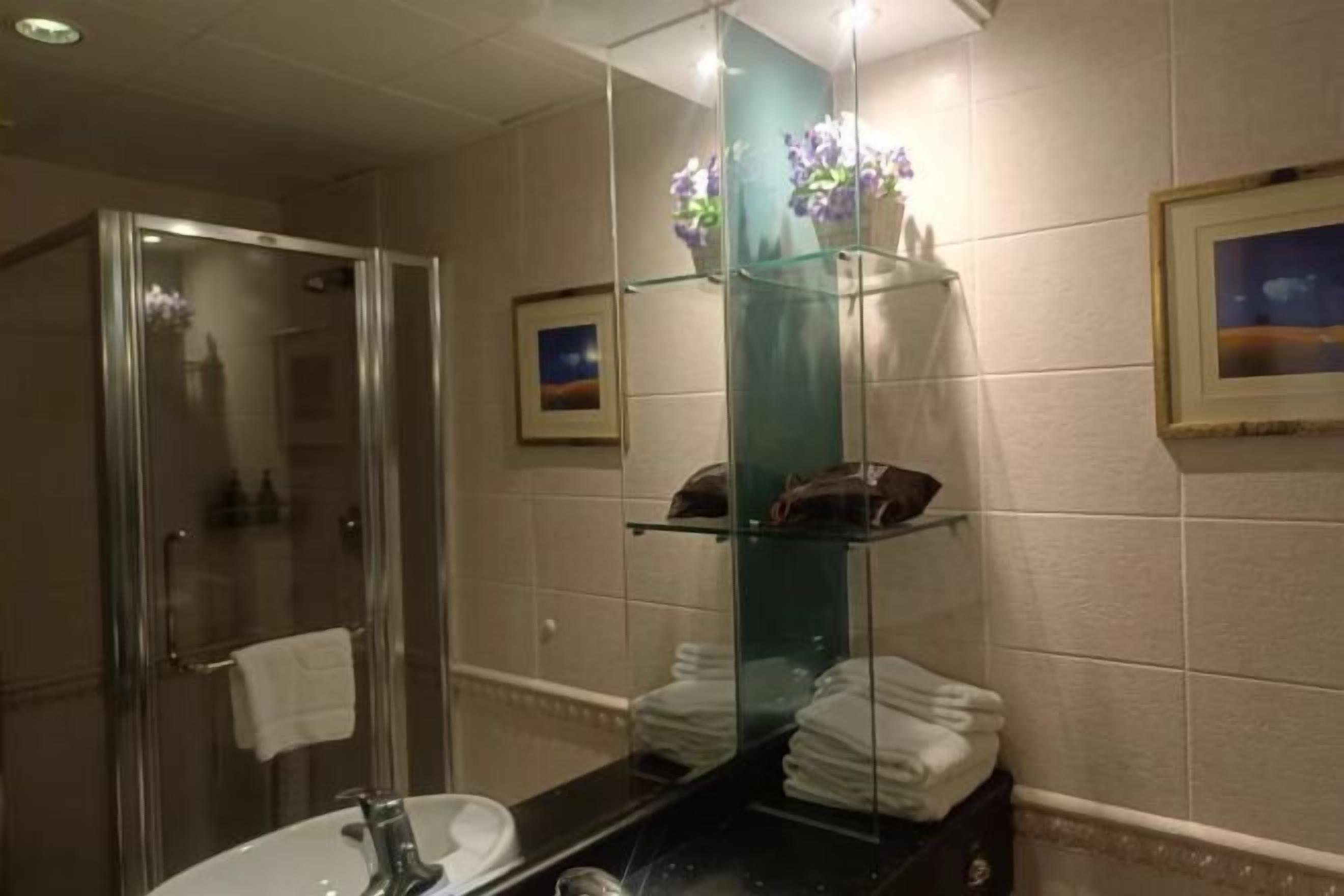 Un baño con cabina de ducha de vidrio, un lavamanos con espejo y repisas con toallas dobladas.