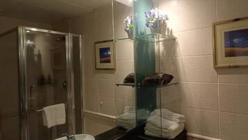 Un baño con cabina de ducha de vidrio, un lavamanos con espejo y repisas con toallas dobladas.
