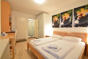 Ein Hotelzimmer mit Doppelbett, einem Holzkopfteil, einem Schreibtisch mit Stuhl, einem Kleiderschrank und einem Duschbereich.