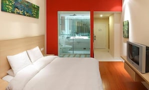 Ein Hotelzimmer mit Bett, Fernseher, einer Glaskabine für das Badezimmer und einer roten Akzentwand.