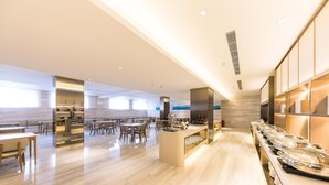 A spacious hotel dining area with a long counter, multiple tables, and a modern interior design.