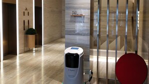 A robot vacuum cleaner in a hotel lobby with a 'No Smoking' sign, a red chair, and a staircase.