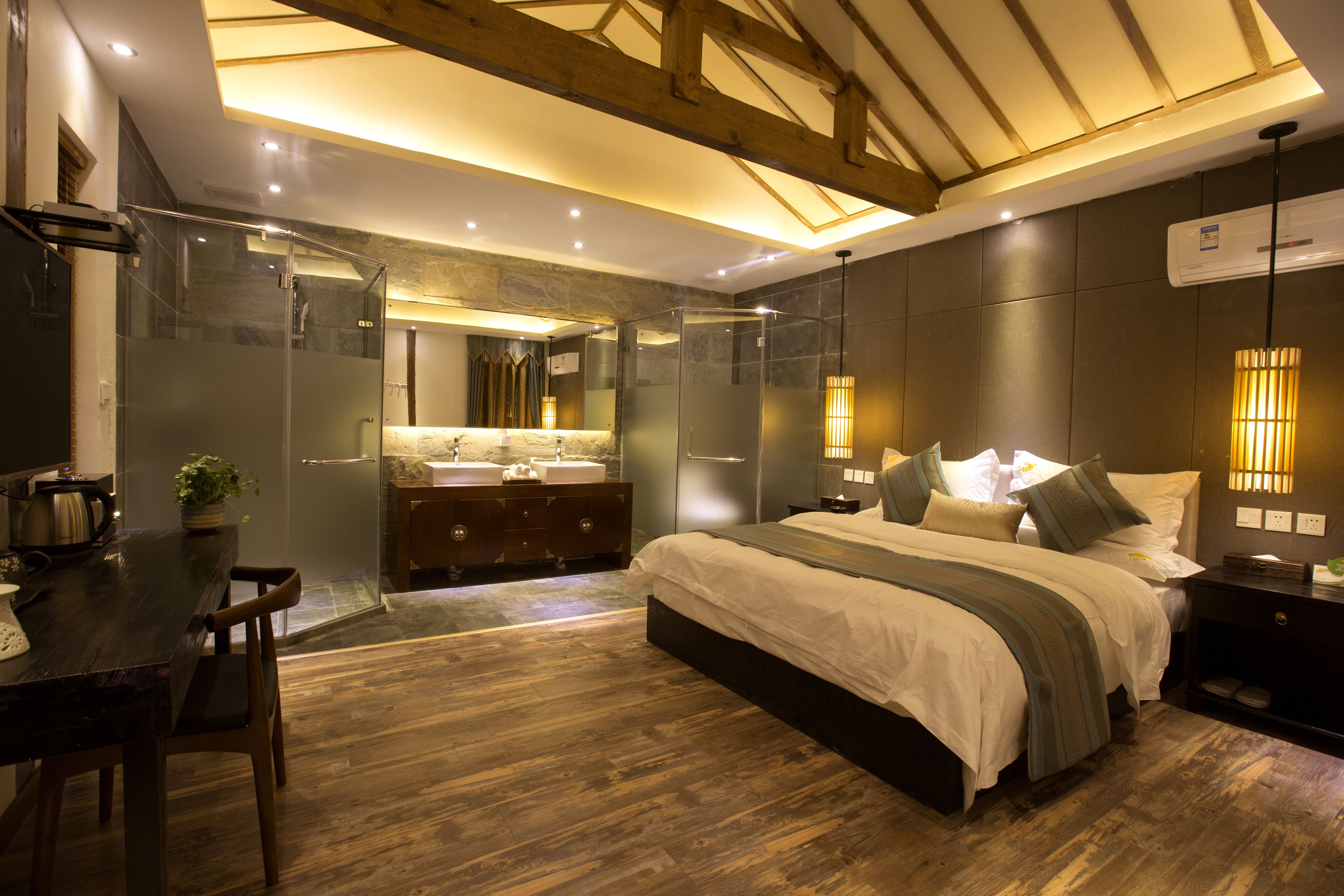 A modern bedroom with a large bed, a wooden dining table, a glass shower enclosure, and a built-in sink.