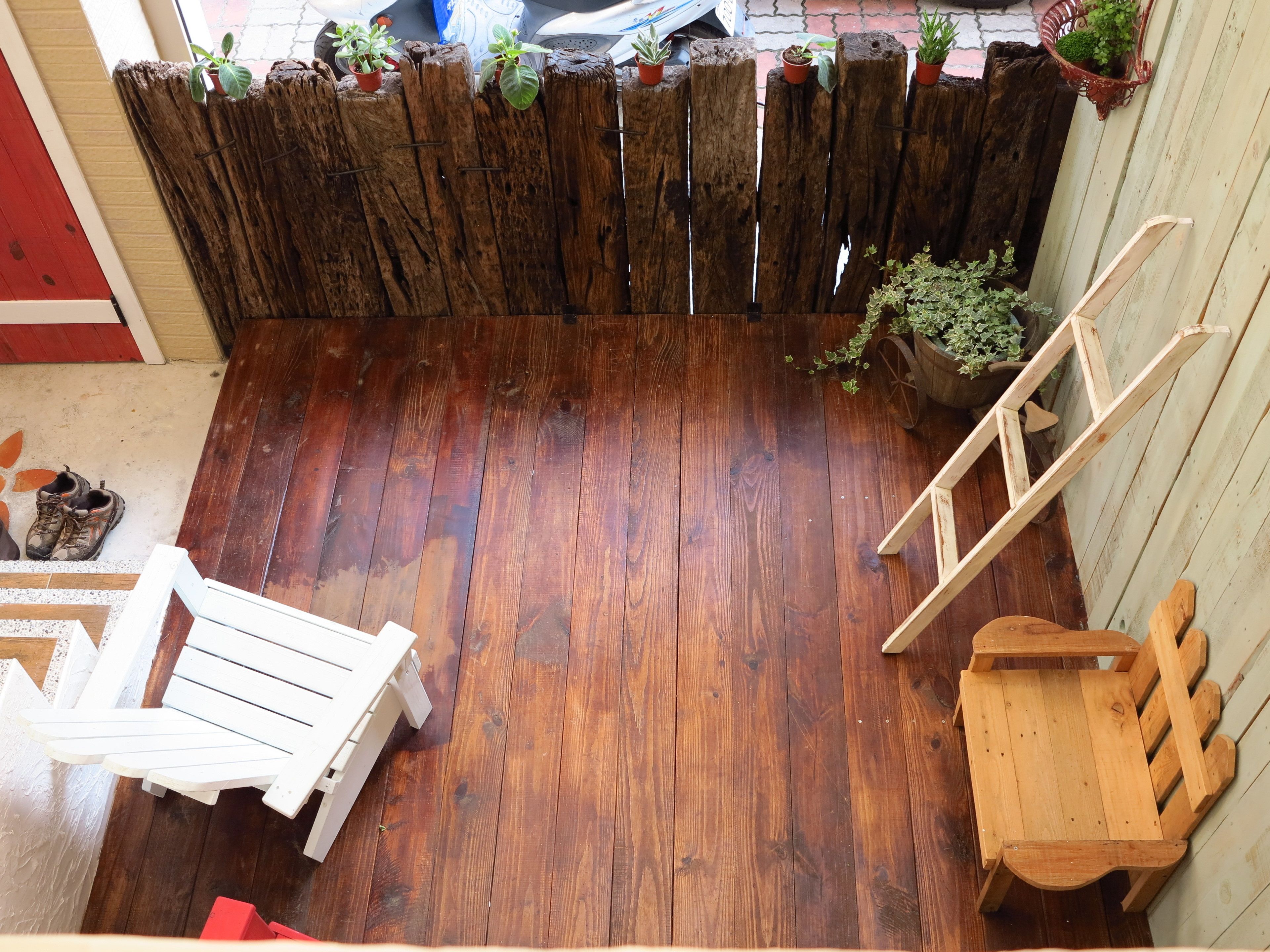 A wooden deck with a wooden fence, potted plants, a white chair, and a wooden bench.
