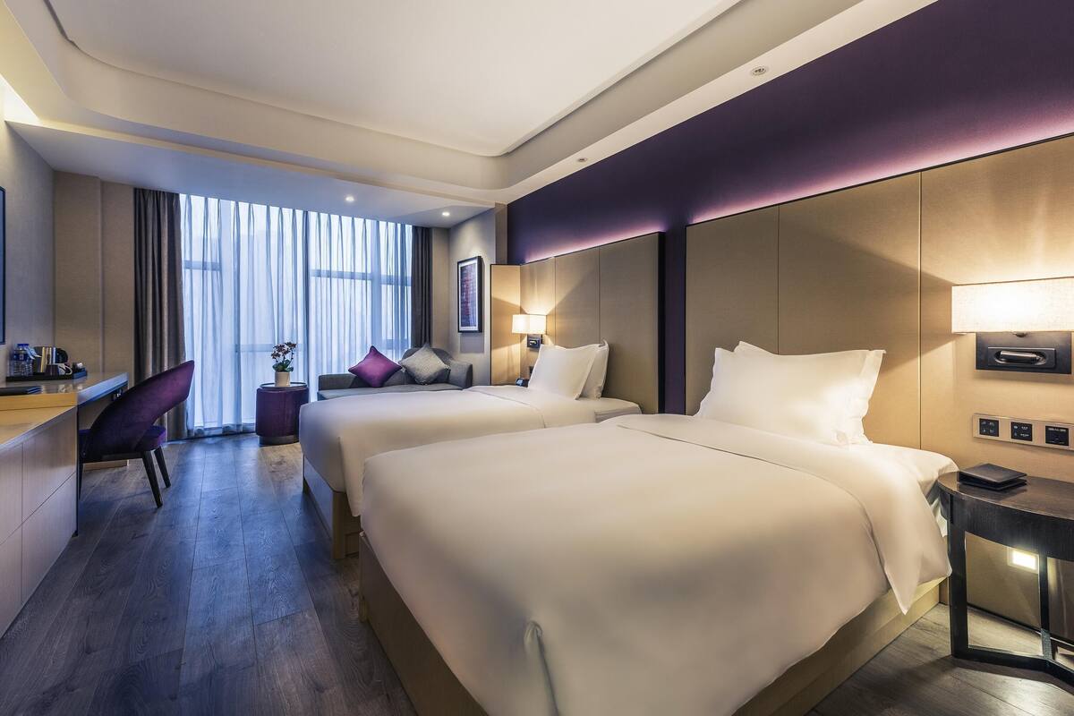 A hotel room with two beds, a desk, a chair, and a window with curtains.