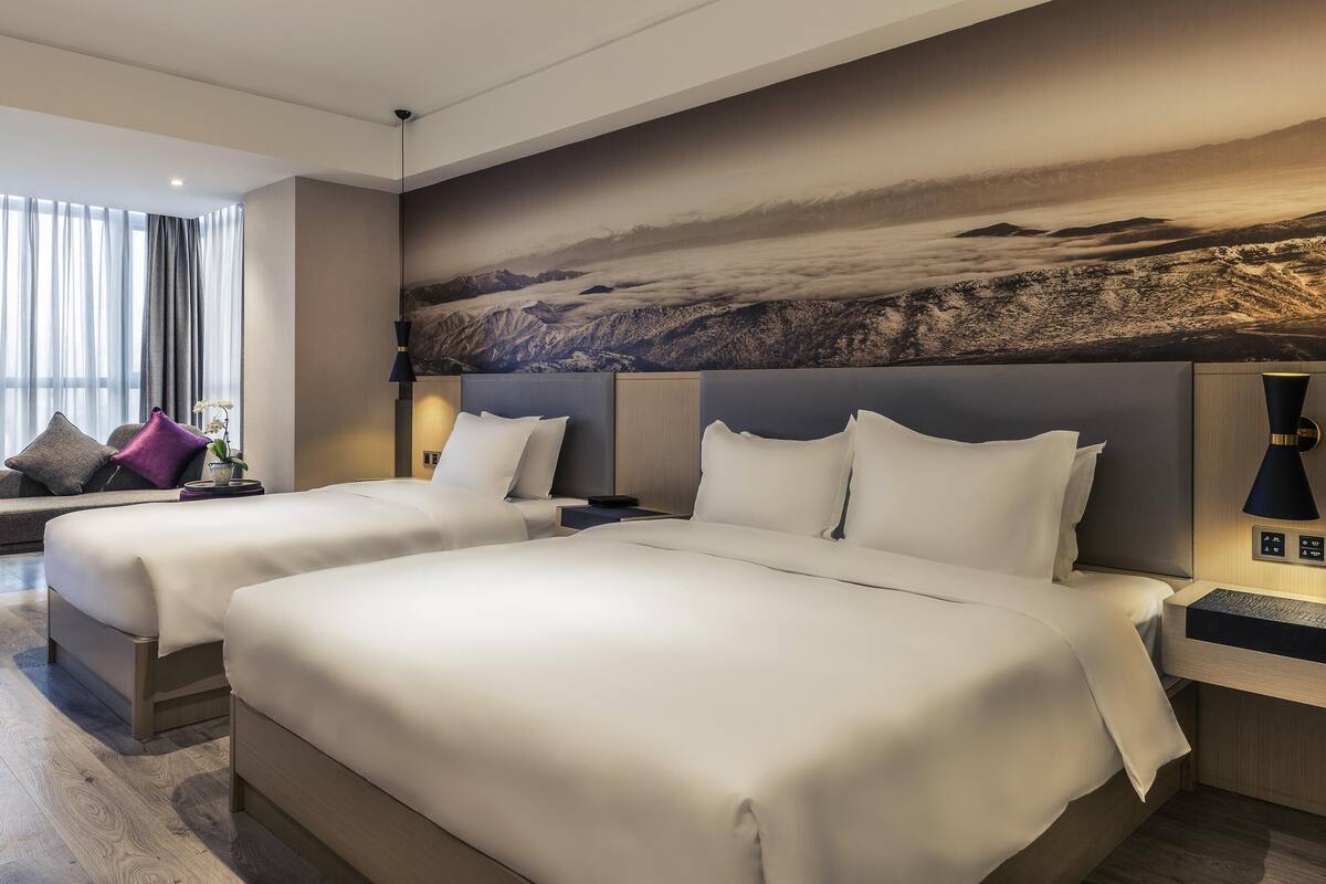 A hotel room with two beds, a large wall mural, and a seating area with a view of the mountains.