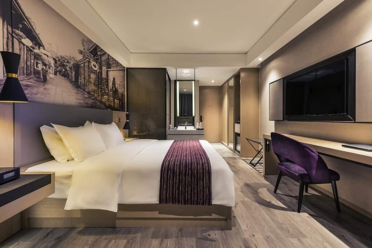 Una habitación de hotel moderna con una cama grande, un escritorio, una silla, un televisor y un mural en la pared.